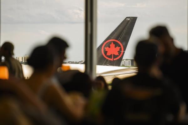 Tail of an Air Canada plan is seen through a crowd of people standing at a window