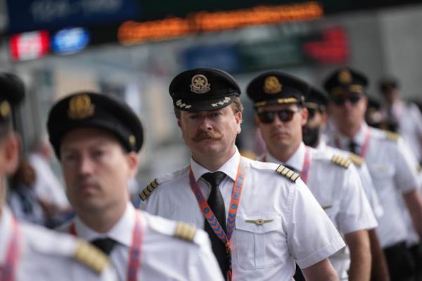 Airline pilots in uniform, seen from the chest up, standing in a line outside an airport