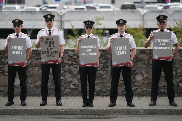 A row of pilots in work uniforms hold up protest signs that say they are 'Strike Ready'